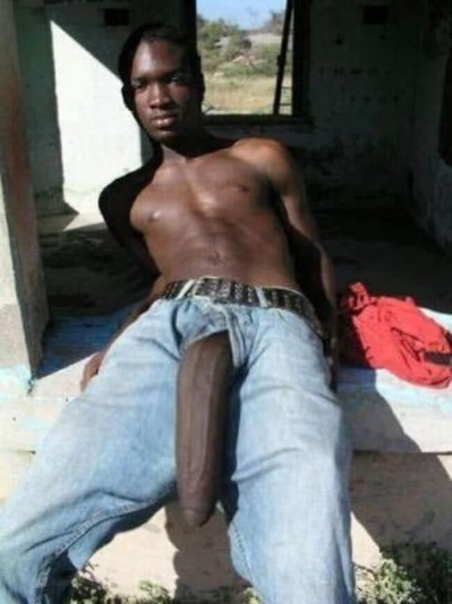 foto de um homem negro deitado com o zíper aberto e com uma pica enome pra fora da calça.