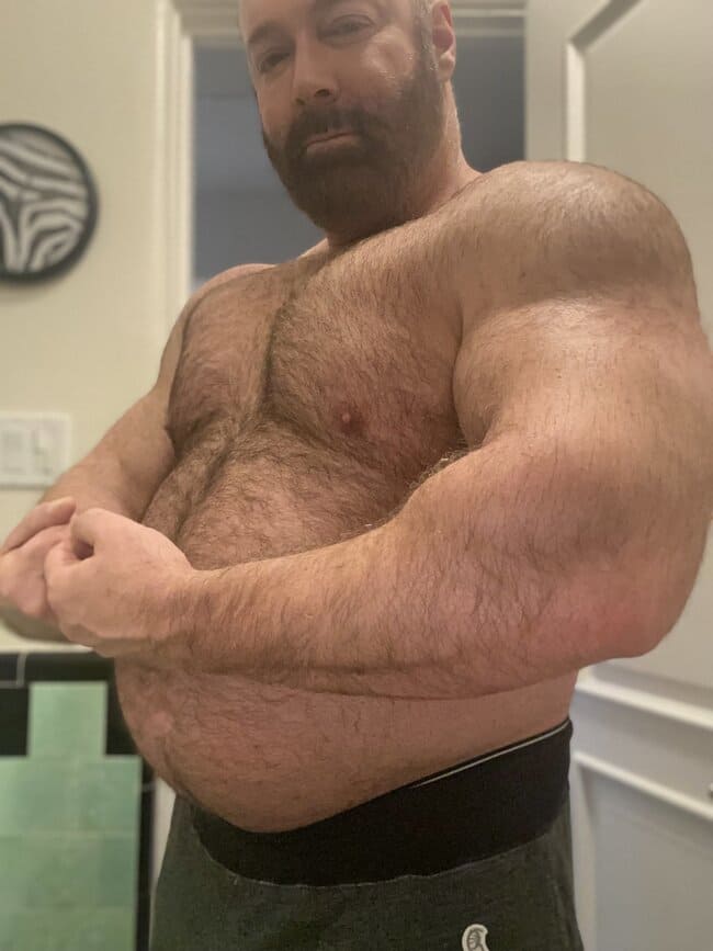 Brad Kalvo usando uma barba cheia, posando pelado e exibindo os musculos fortes dos braços